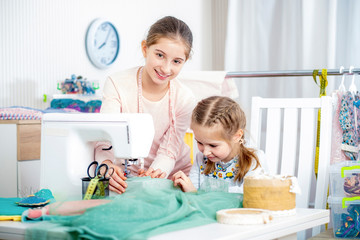 Smiling happy sister teaches a little girl to sew on a sewing machine by herself