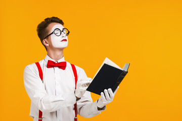 portrait of mime man artist reading book isolated on yellow background. copy space for text