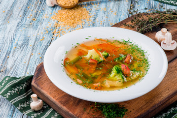 Vegetable broth/soup with broccoli, asparagus, carrots, onions, bell peppers and greens in a white plate on a wooden blue background in a beautiful composition. Close up