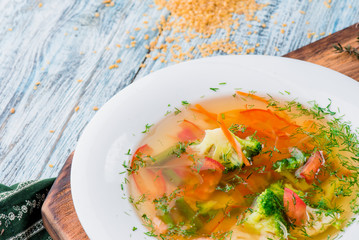 Vegetable broth/soup with broccoli, asparagus, carrots, onions, bell peppers and greens in a white plate on a wooden blue background in a beautiful composition. Close up