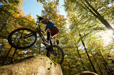 Professional sportsman cyclist riding on back wheel on trial bicycle, man biker making acrobatic...