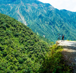 Fototapeta na wymiar Man taking a bike at the edge of the Bolivian death road on the background of forested mountains
