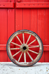 Antique vintage wooden wheel against a red door