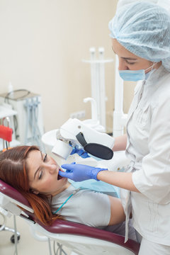Attractive smiling woman doctor in a white uniform with tools in hand. Young beautiful female dentist takes jaw x-ray of female patient. Attractive woman patient at dentist taking x-ray exam.