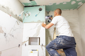 Plumber using electric screwdriver. Bathroom renovation concept. Marble ceramic tiles with spacers...