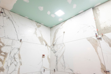 Bathroom renovation concept. Marble ceramic tiles with spacers and grey cement walls in bathroom, renovating and working in toilet, space for text. Repairing