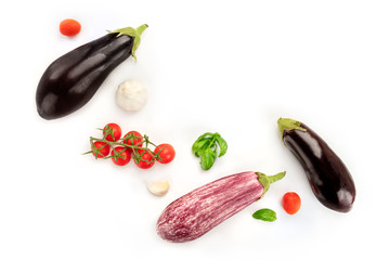 A flat lay composition with vegetables. Eggplants, tomatoes, basil leaves, and garlic, shot from the top on a white background with copy space