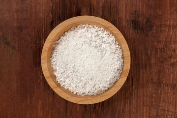 Fototapeta na wymiar A bowl of sea salt, shot from the top on a dark rustic wooden background