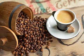 Scattered coffee beans, a cup of espresso, pieces of chocolate with nuts on a wooden board.