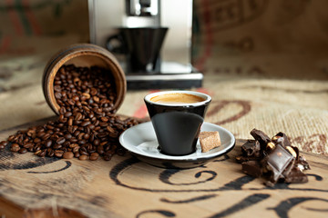 Scattered coffee beans, a cup of espresso, pieces of chocolate with nuts on a wooden board.