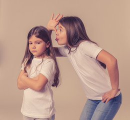 Older sister making funny faces and sticking out tongue to her younger angry sister