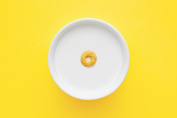 Cereal loop floating on a white bowl full of milk on yellow background. Close up top down view.