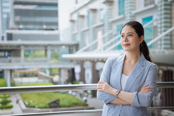 Fototapeta na wymiar confident smiling young beautiful asian woman manager looking at blue sky leaning on railing on balcony in break time. real moments concept. elegant office lady relax outdoor from work company city