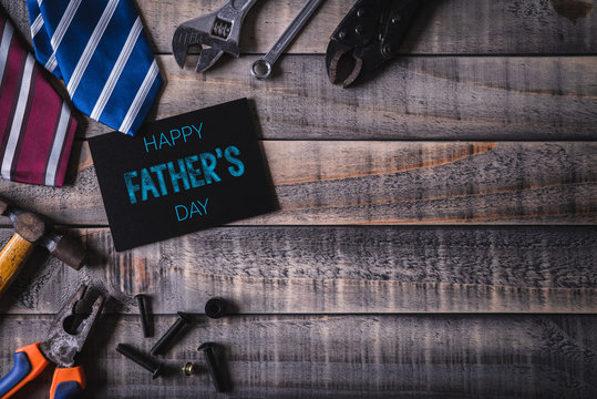 Happy fathers day concept. Top view of white picture frame with border of tools and ties, retro film camera on dark wooden table background. Flat lay.