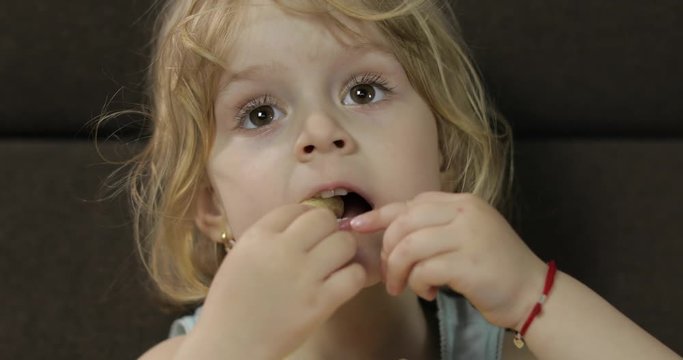 Girl sitting on sofa and eating corn puffs. Child smiling and taste puffcorns