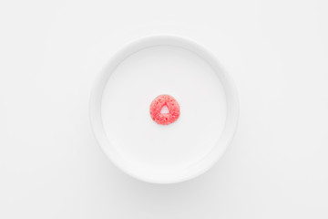 Single cereal ring floating on a white bowl full of milk on white background. Close up top down view.