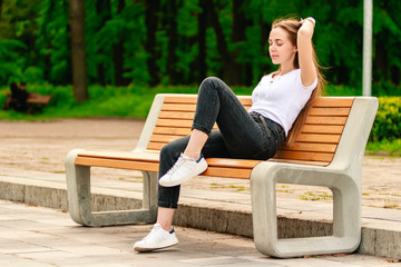 A young girl is resting on the wooden bench in the park