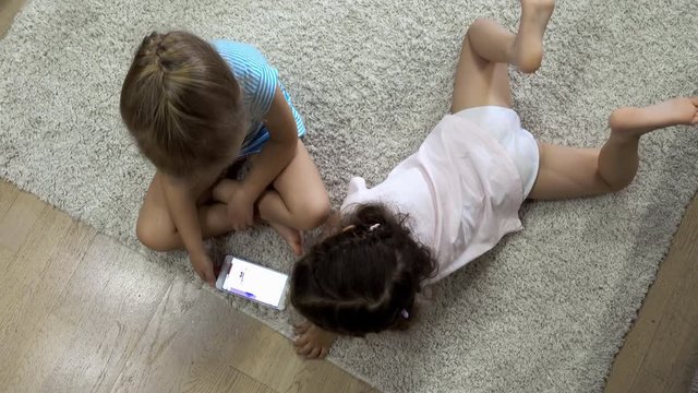 Little girls are lying on the floor and playing with the gadget