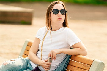 Young attractive girl wearing sunglasses and resting on a bench