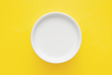 Milk in a white bowl on yellow background. Close up top down view