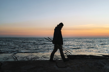 Silhouette of man fisherman wearing coat, holding rod