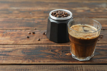 Glass of fresh coffee and coffee beans on wooden table, space for text