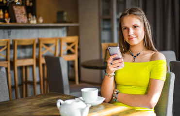 portrait of young teenager brunette girl with long hair sitting indoor in urban cafe and use her smartphone