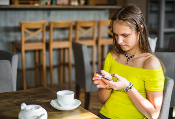 portrait of young teenager brunette girl with long hair sitting indoor in urban cafe and use her smartphone