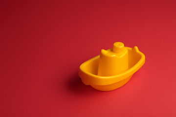 little yellow plastic toy ship on the red background with copy space.