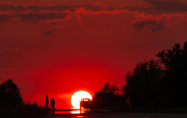 Solar disk and silhouettes of car and people against the background of the red sunset sky