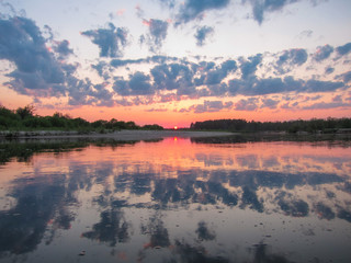 Red decline under the forest river with reflection of clouds in the river