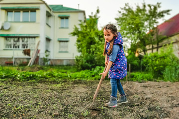 Little girl on a sunny day in the garden with a hoe