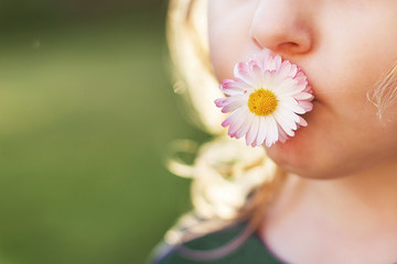 Obraz na płótnie Canvas girl with a daisy flower in her mouth on a green background close. lips with flower on grass background. portrait of a little girl