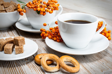still life white Cup with coffee and pieces of cane sugar with bagels on a vintage wooden table with bunches of Rowan.