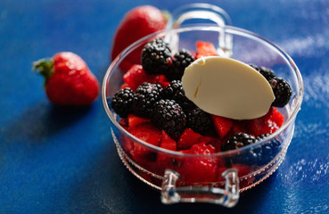 Fresh sweet brightly red berry strawberry in a glass cup on a blue background with dense cream. Ready photo background. Soft focus. Macro.
