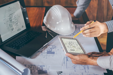 Construction engineering or architect discuss a blueprint while checking information on drawing and...