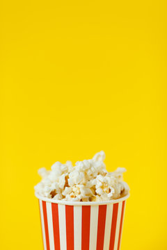 Fresh tasty popcorn and cup on color yellow background, side view with space for text. Cinema snack close-up