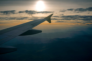 Plakat Lowkey image of airplane wing in the sky over mountains. Spectacular view of a sunset above the mountains. Aerial shot from airplane window.