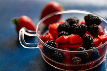 Fresh sweet brightly red berry strawberry in a glass cup on a blue background with dense cream. Ready photo background. Soft focus. Macro.