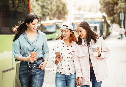 Happy Asian girls using mobile phone outdoor - Young millennial people having fun with new smartphone app technology - Concept of friendship, social, tech and teenager lifestyle