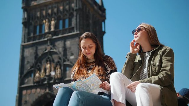 Two women sitting on a background of Bridge Tower of Charles Bridge holding a map