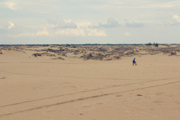 Fototapeta na wymiar Sand dunes, dry grass, white clouds on the blue sky on the horizon, in the distance the boy walks in the sand .