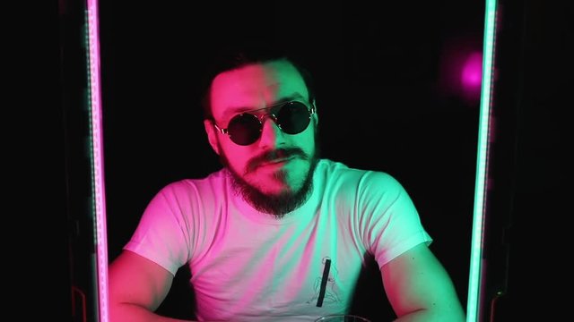 Portrait of attractive cheeky man in sunglasses looking at camera in neon lights in the nightclub.
