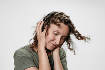 Fototapeta premium Carefree cheerful young curly woman listen favourite music with hand on her headphones