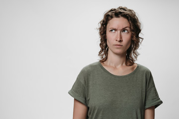 Young curly woman with puzzled raises eyebrows negative facial expression
