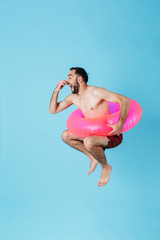 Photo of attractive shirtless tourist man wearing rubber ring smiling while swimming and jumping