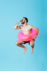 Photo of masculine shirtless tourist man wearing rubber ring smiling while swimming and jumping