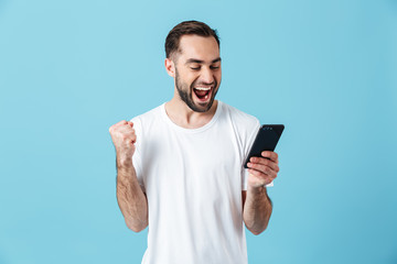 Photo of attractive brunette man wearing basic t-shirt laughing and holding smartphone