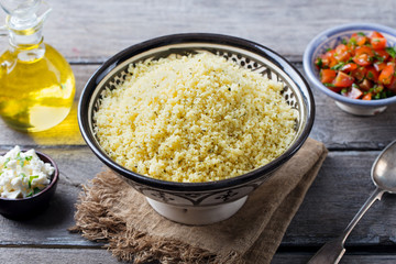 Couscous in bowl with olive oil. Wooden background. Close up.