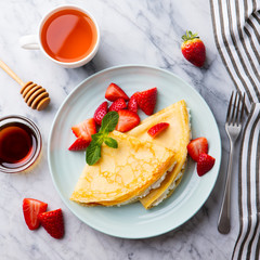 Crepes, thin pancakes with cream cheese, ricotta and fresh strawberries. Marble background. Top view.